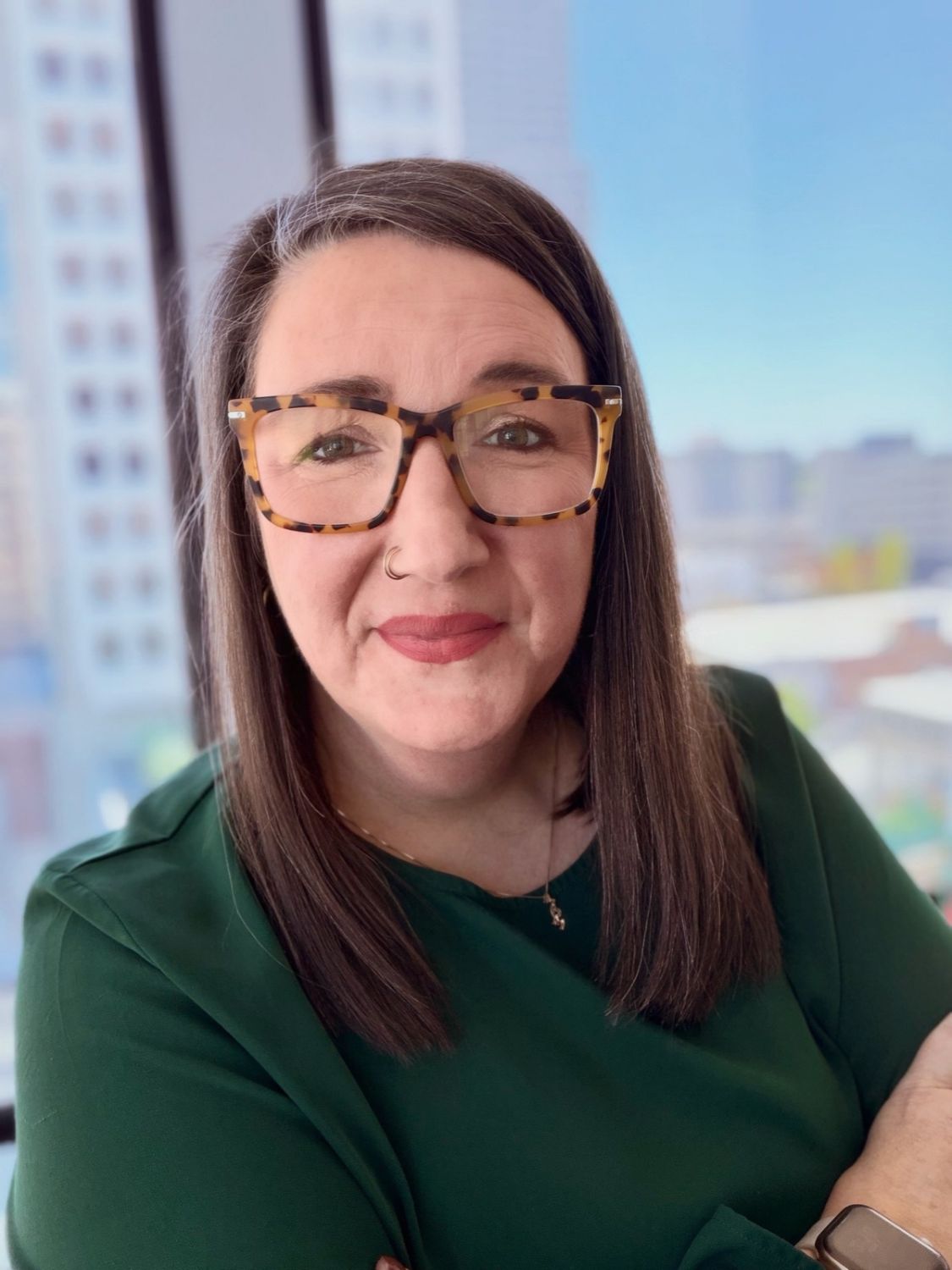 A woman with long brown hair wearing tortoise-shell glasses and a green top.